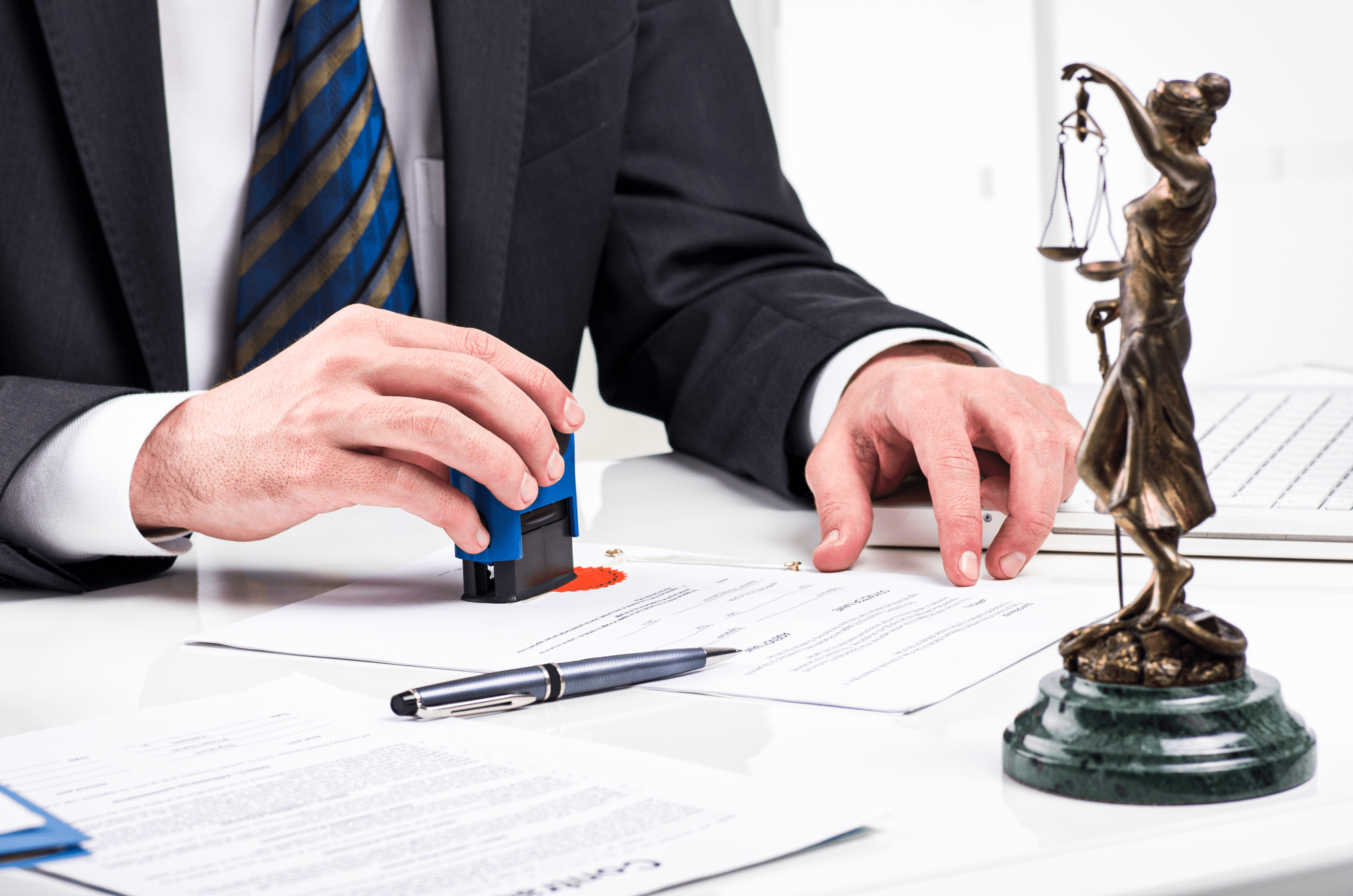 A businessman stamps documents on a desk with a Lady Justice figurine nearby, symbolizing legal authentication and professionalism.