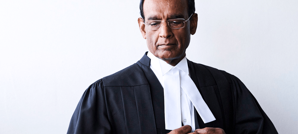 A solemn lawyer in formal black robes and a white collar, thoughtfully adjusting his attire against a neutral background. This image conveys professionalism in law.