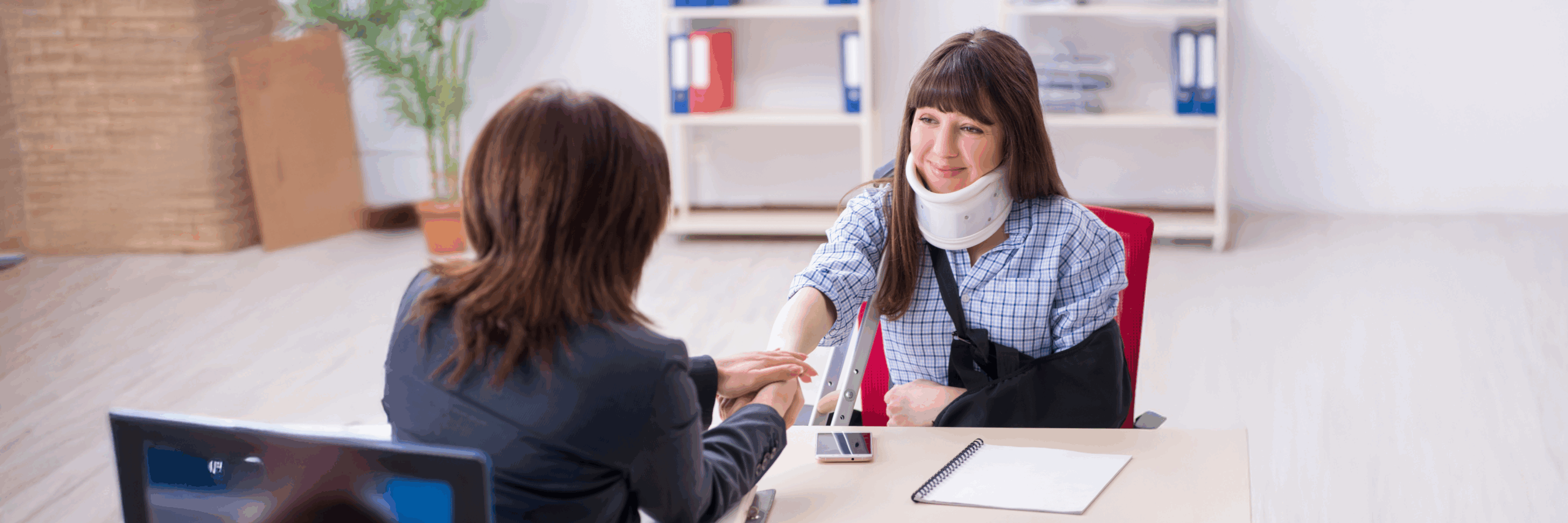 A woman with a neck brace and arm in a sling smiles as she shakes hands with a seated professional, discussing her recovery in a bright office.
