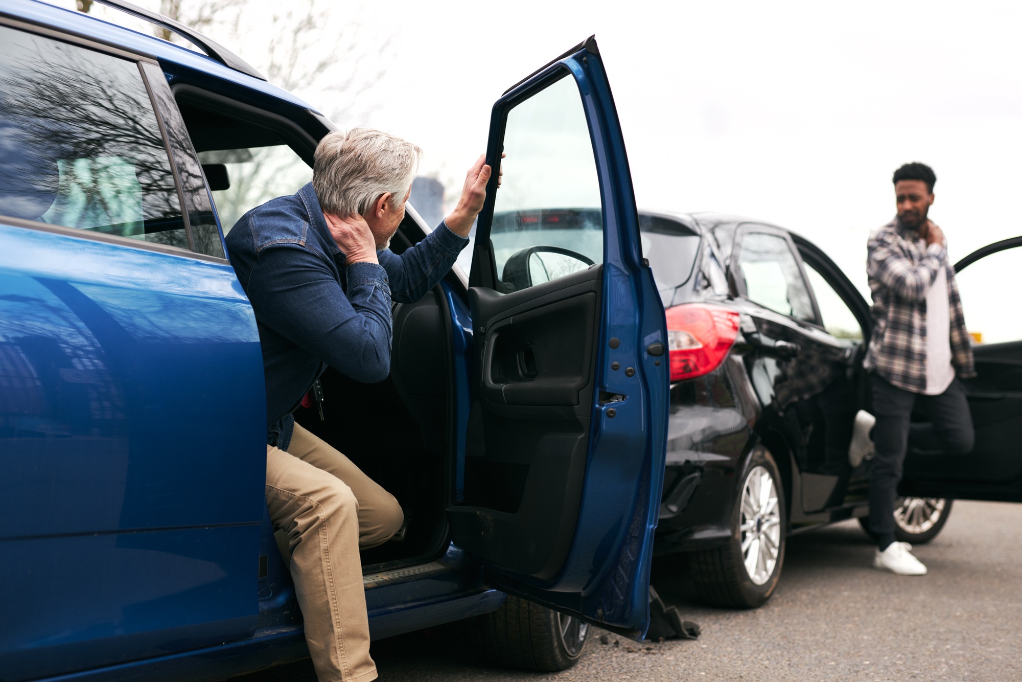 Senior and younger male drivers get out of cars