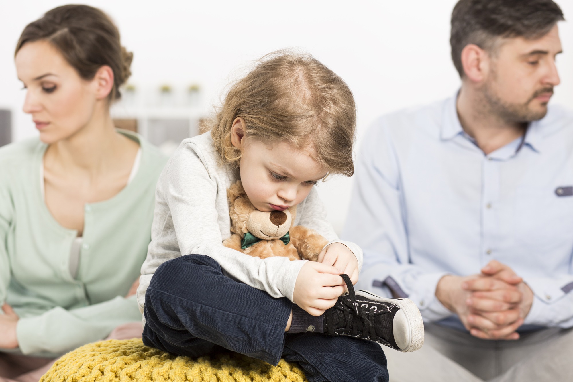 Photo of a gloomy young family with a sad little boy hugging a teddy bear, and his parents with depressed looks